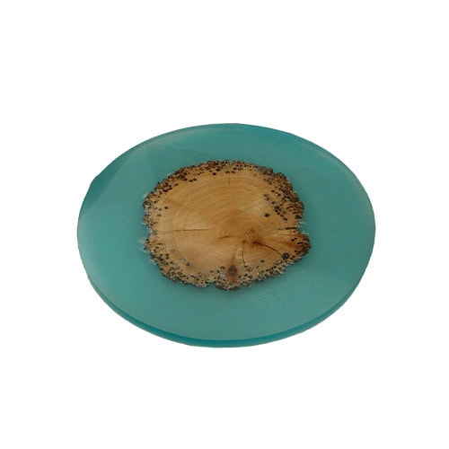Susanna Island Accessory shows a circular piece with natural wood preserved in turquoise resin. The design recalls a floating island, combining earthy texture with vivid color clarity.