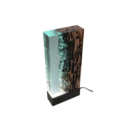 Water Brick Lamp pairs dark textured wood with glowing resin, evoking the movement of water within a solid form. Its clean rectangular shape offers both function and sculptural beauty.