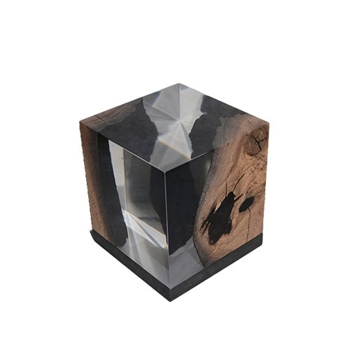 Wetland Lamp is a sculptural cube of resin and dark wood that refracts light with crystalline clarity. Organic inclusions enhance its raw elegance, making it both functional lighting and a statement object.