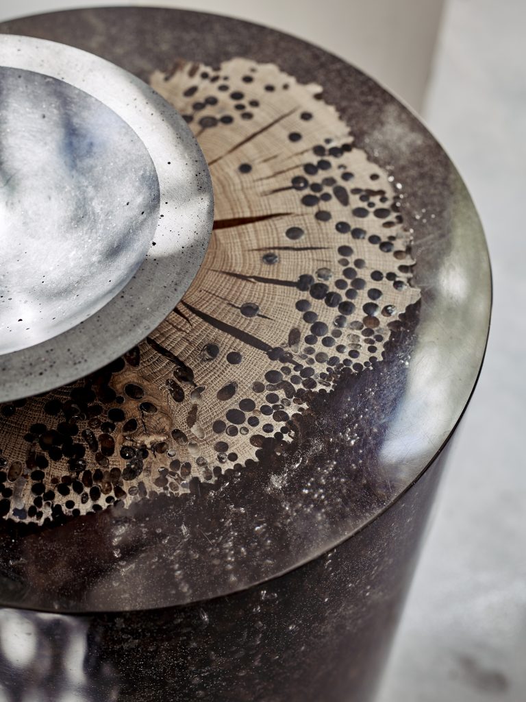 Closeup of Fisheye Stool/Side Table with a rounded shape, made of solid wood with a natural finish, set against a gray background.