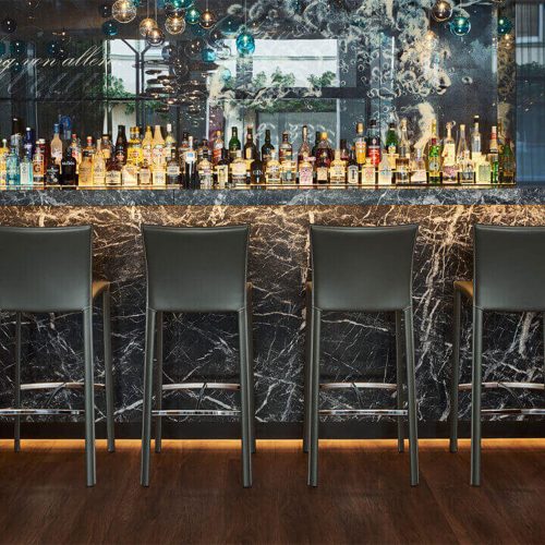 four bar stools made with steel legs and upholstered in dark gray leather
