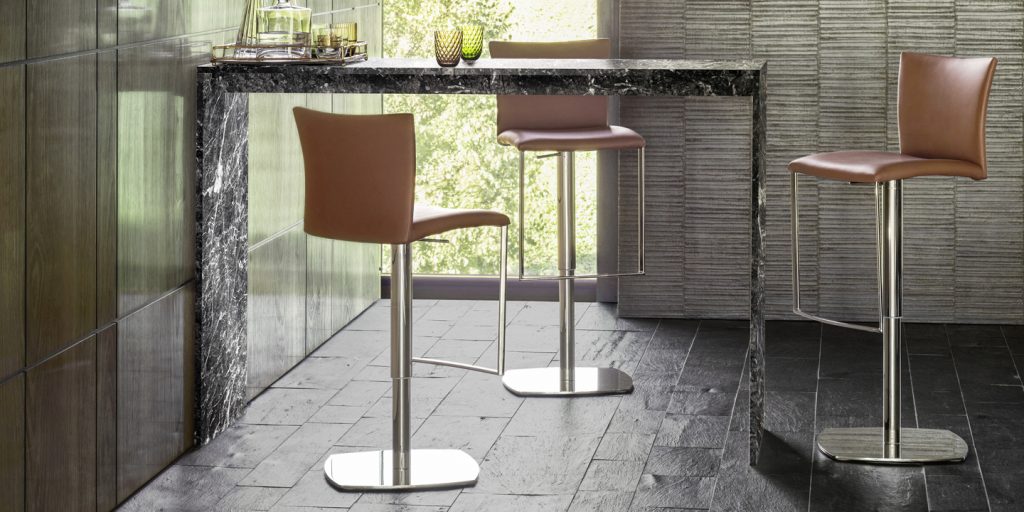 Three bar stools made of chrome on its base and upholstered in beige leather on a white background