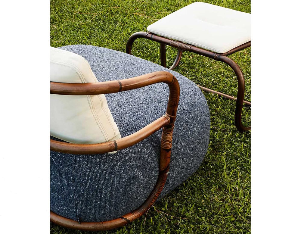 A close-up of the Jungle Armchair featuring a plush blue cushion a curved wooden frame and a matching ottoman set on a grassy surface