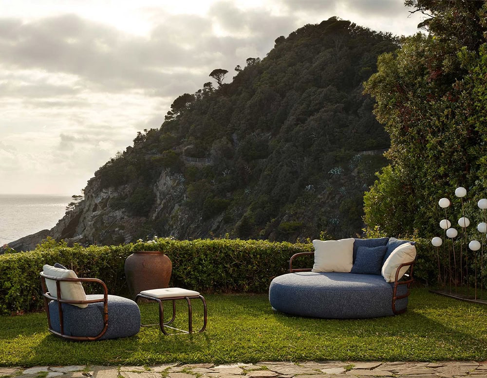 A serene outdoor lounge featuring the Jungle Armchair with plush modern seating small tables lush greenery and a stunning mountain view