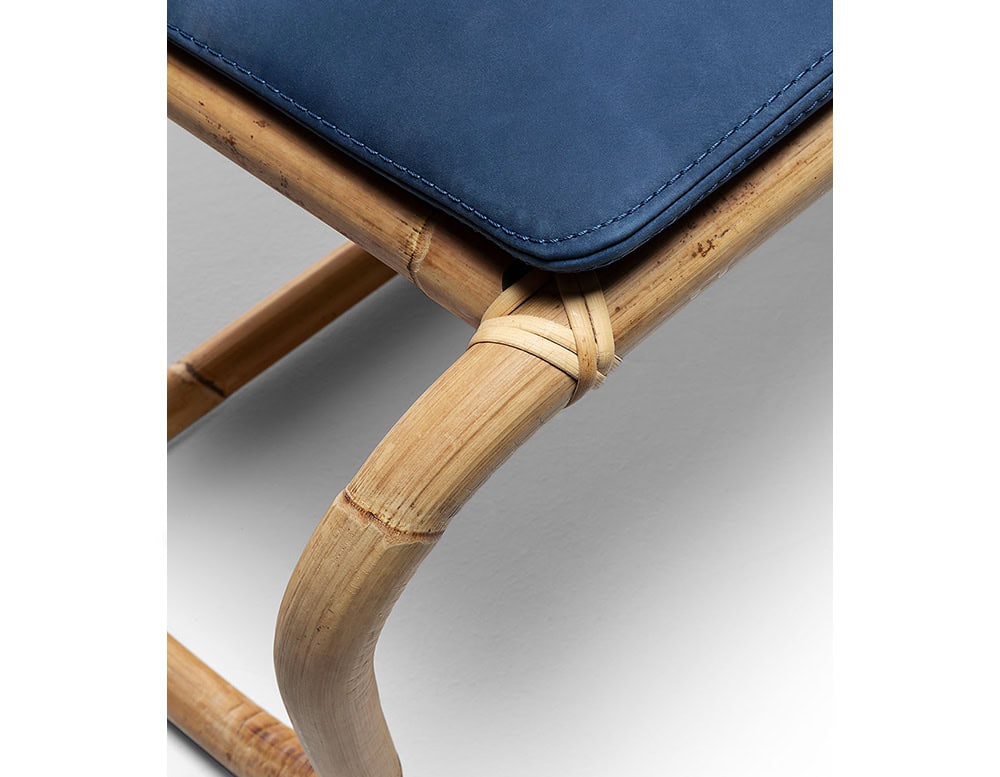 Closeup of Jungle Pouf upholstered in blue fabric and brown wooden structure on a white background.