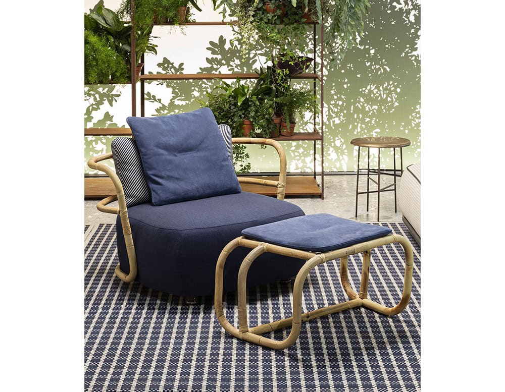 Jungle Pouf upholstered in blue fabric with a blue cushion and brown wooden backrest in a living room.