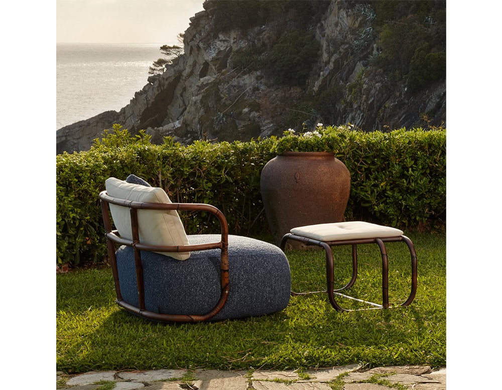 Jungle Pouf upholstered in gray fabric with a white cushion and brown wooden backrest on a garden.