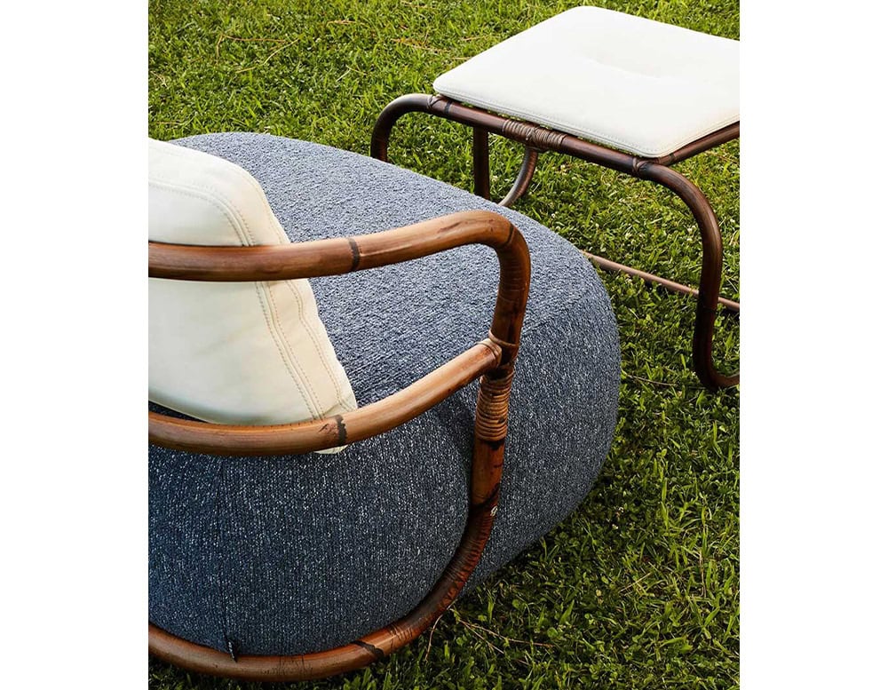 Jungle Pouf upholstered in gray fabric with a white cushion and brown wooden backrest on a garden.