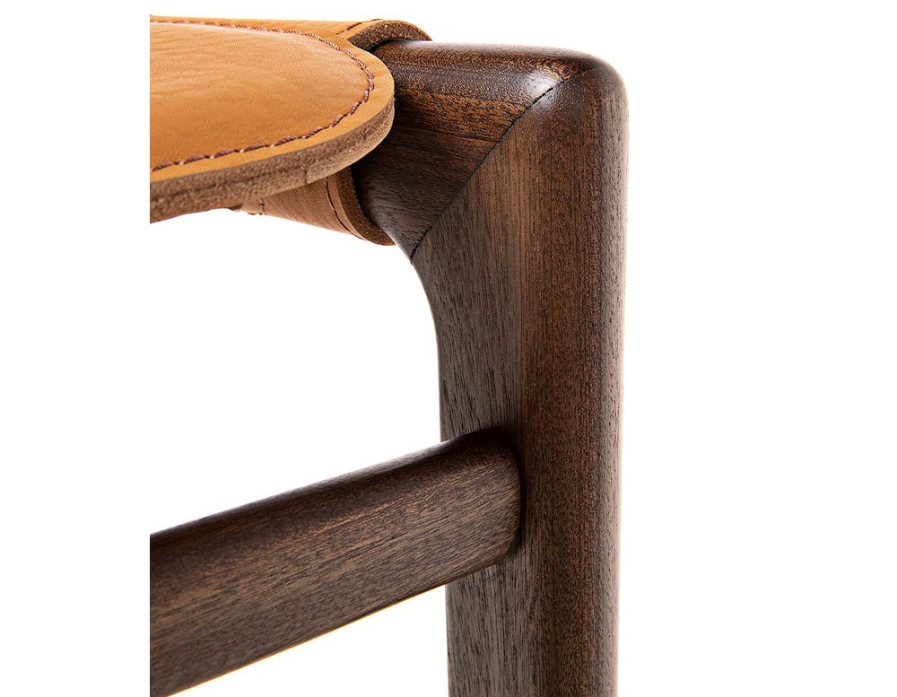 Closeup of Levante Stool. Structure in brown wood, seat in orange leather on a white background.