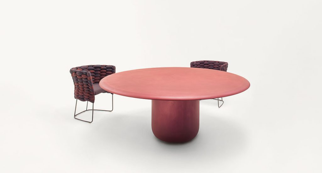 Two red and black Ami Indoor Chairs, structure upholstery of woven fabric, seat cushion of fabric, structure and leg in steel next to a table on a white background.