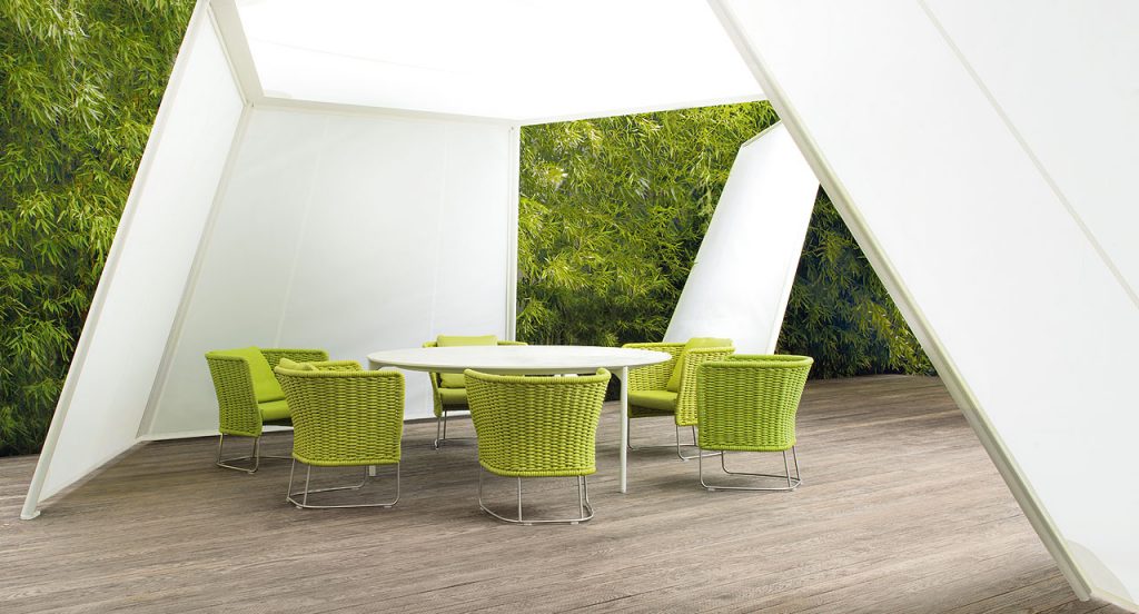 Ami Outdoor Chair: Six green woven chairs with a curved backrest on a terrace.