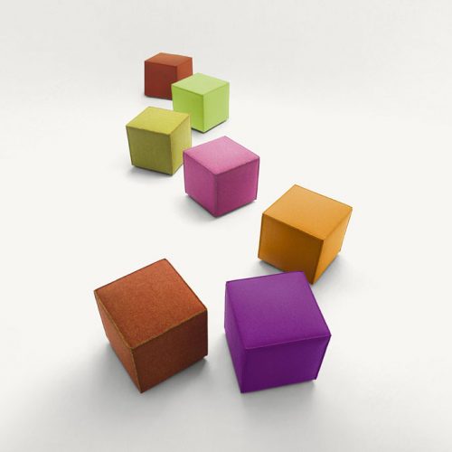 Seven Cubo pouf, one in purple, one in pink, one in brown, one in red, one in orange, one in green and one in yellow on a white background.