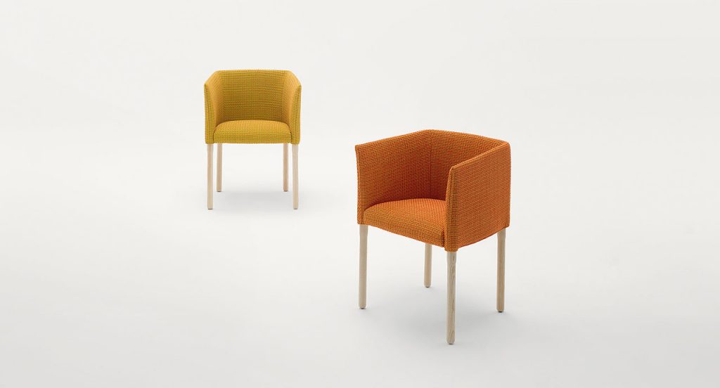 Two Elsie Chairs with armrest, upholstery in fabrics, one in yellow and one in orange, legs in natural heartwood on a white background.