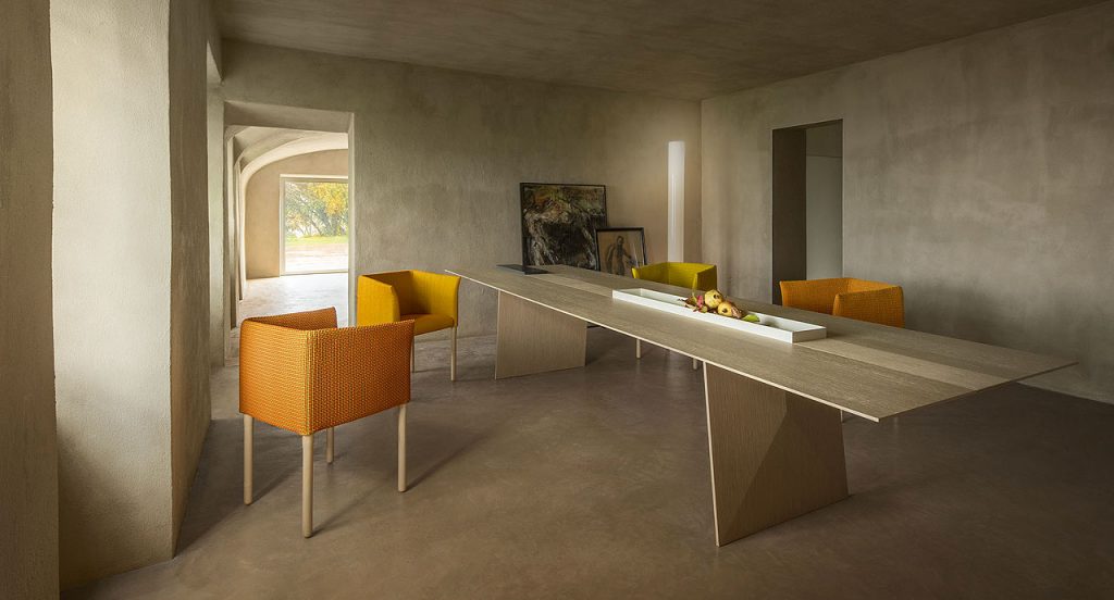 Four Elsie Chairs with armrest, upholstery in fabrics,two in orange and two in yellow, legs in natural heartwood in a dining room.