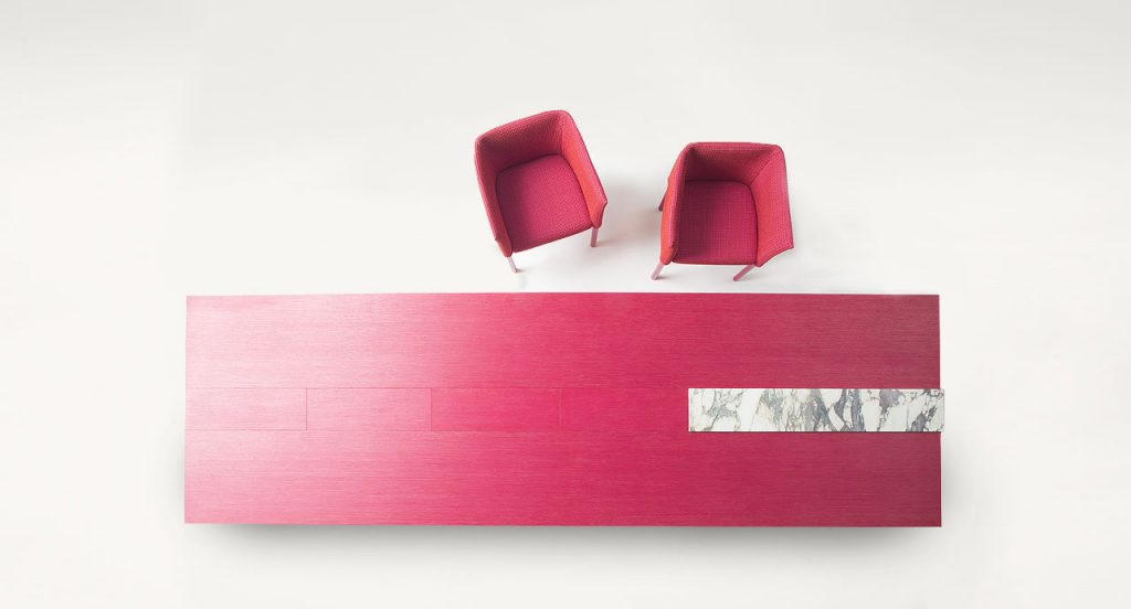 Two Elsie Chairs with armrest, upholstery in red fabrics, legs in natural heartwood in a dining room.