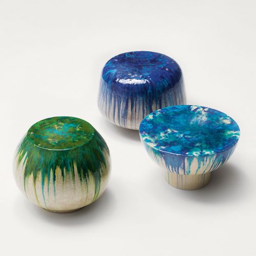 Three beige Calatini side tables with abstract shape, falling paint pattern, two in blue and one in green on a white background.