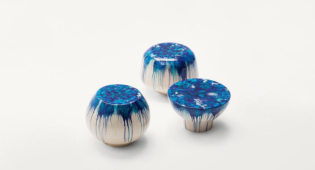 Three beige Calatini side tables with abstract shape, blue falling paint pattern on a white background.