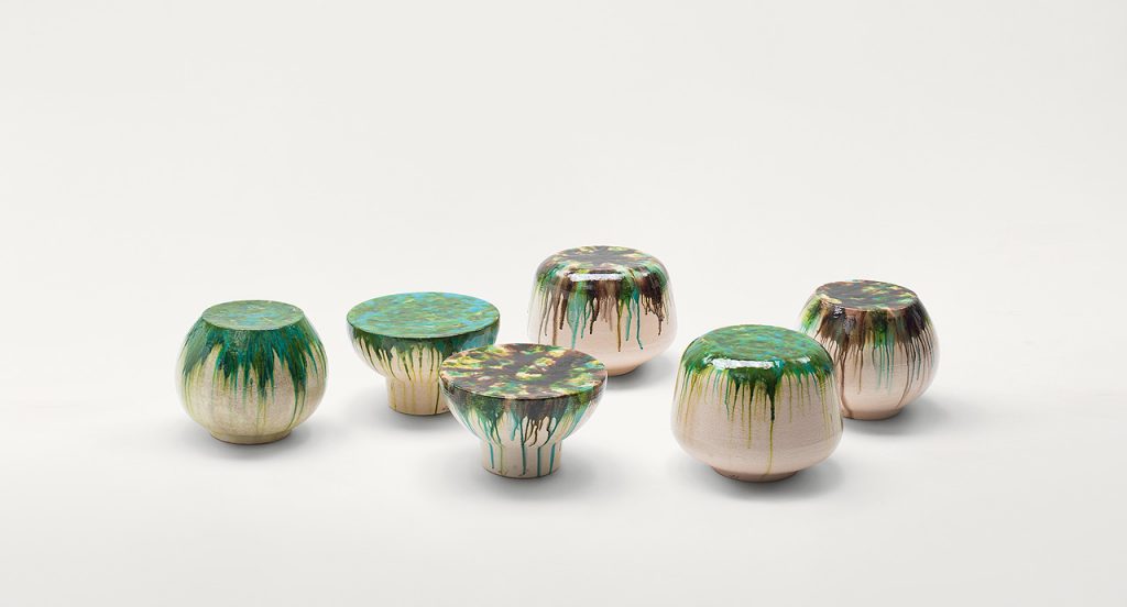 Six beige Calatini side tables with abstract shape, falling paint pattern, three in blue and brown and three in green and blue on a white background.