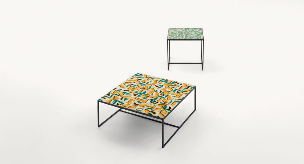Two Cocci side tables, black steel frame, square ceramic top, one in yellow, blue, white and brown and one in green and yellow on a white background.