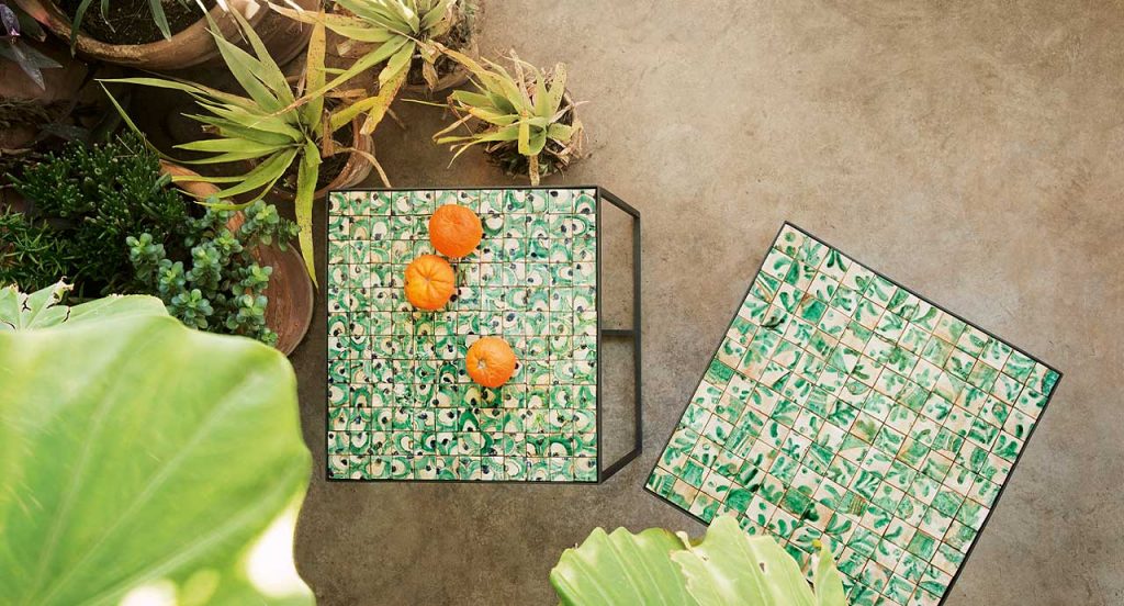 Two Cocci side tables, black steel frame, square ceramic top in green and white in a garden.