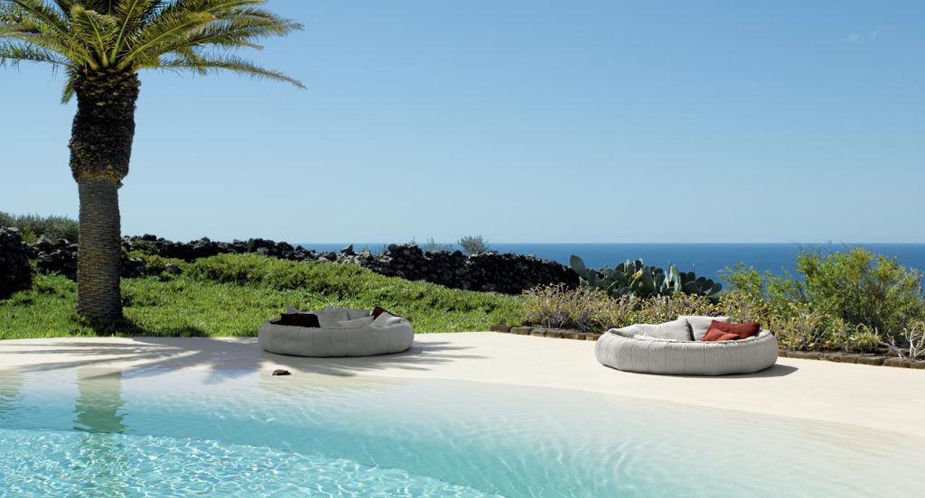 Two Ease round seatings, upholstery in white next to a pool.