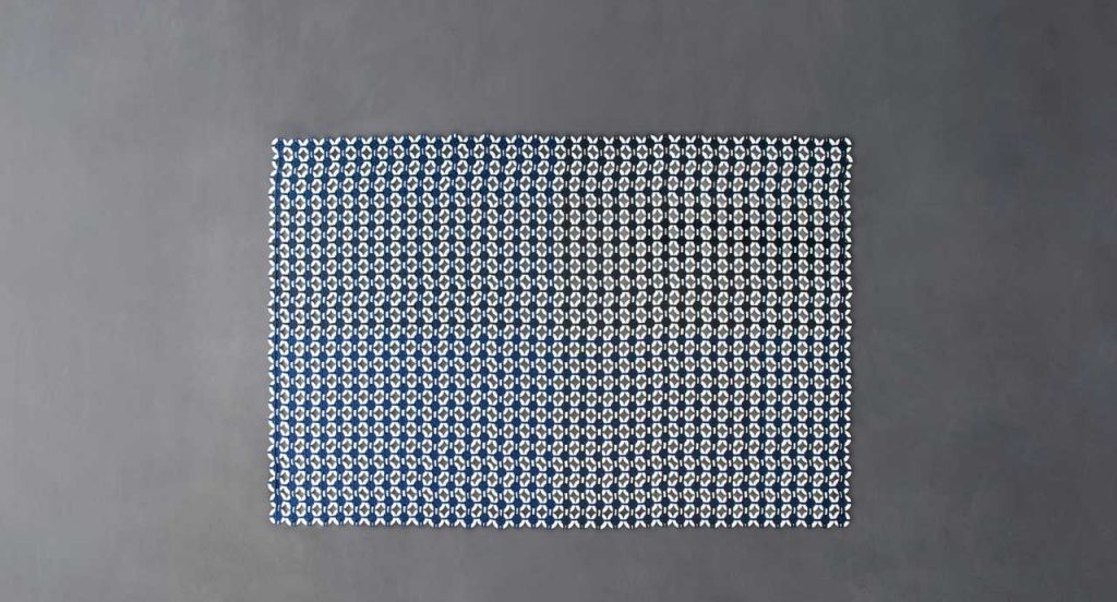 Loom rug made of white plastic rings and blue rope braids on a gray background.