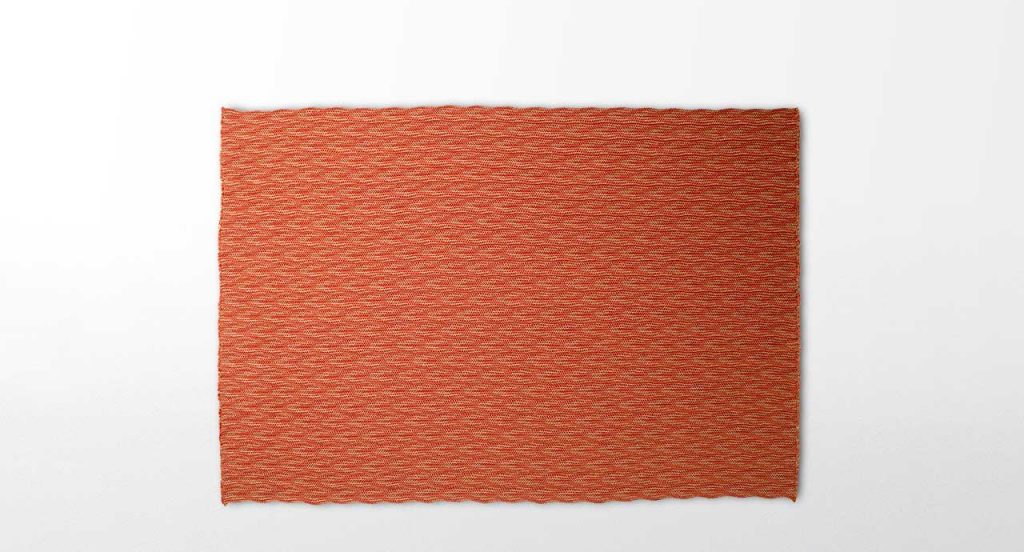 Marea rug, made of braids shaped like waves in red Rope yarn on a white background.