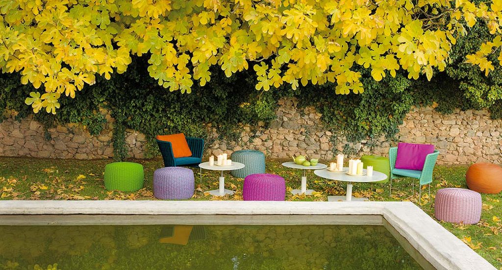 Seven Nido Poufs, upholstery of rope cord, two in green, two in purple, one in pink, one in blue and one in orange in a garden.