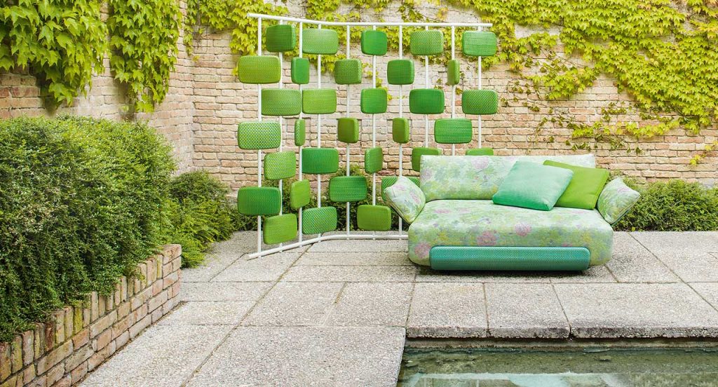 Oasi single seating with backrest and armrest in green and pink leaves and flowers fabric pattern in a garden.