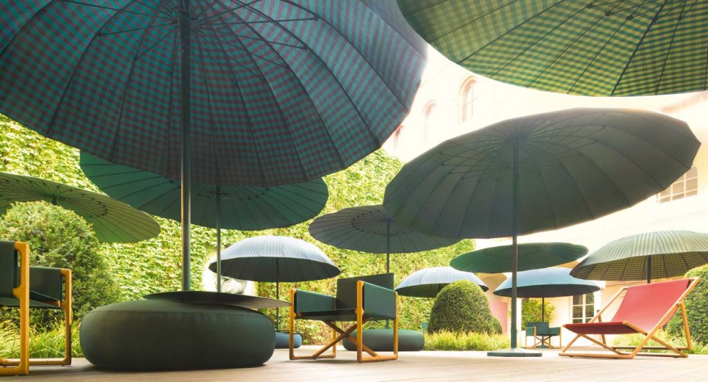 Three Portofino Outdoor Chairs with armrests and little armchair, structure and chair in natural heartwood, upholstery in blue fabric in a garden.