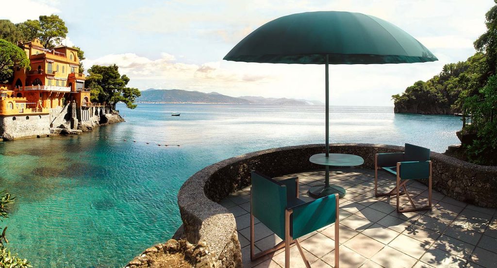 Two Portofino Outdoor Chairs with armrests and little armchair, structure and chair in natural heartwood, upholstery in green blue fabric in a terrace.