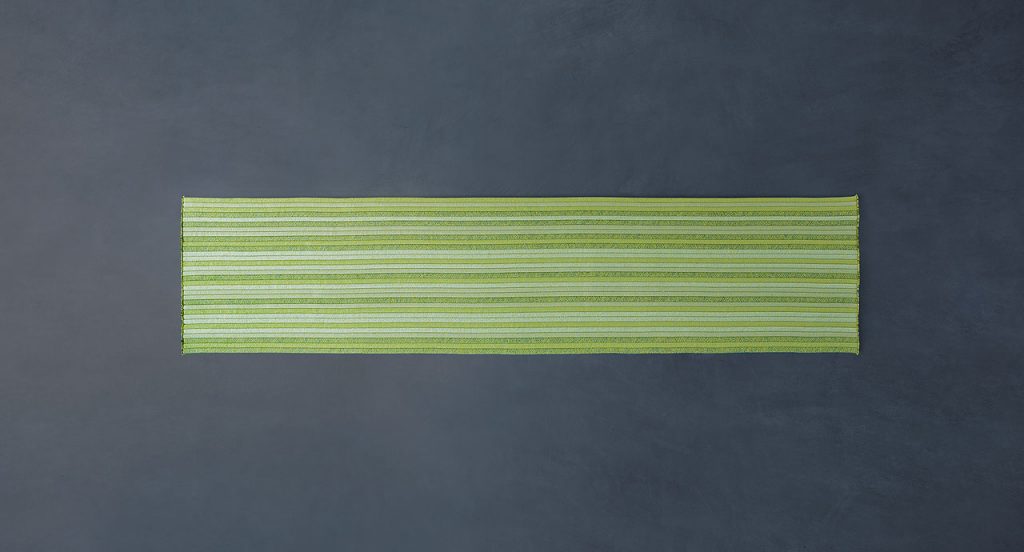 Samo rug made of yellow and green rope cords and irregular shape on a grey background.