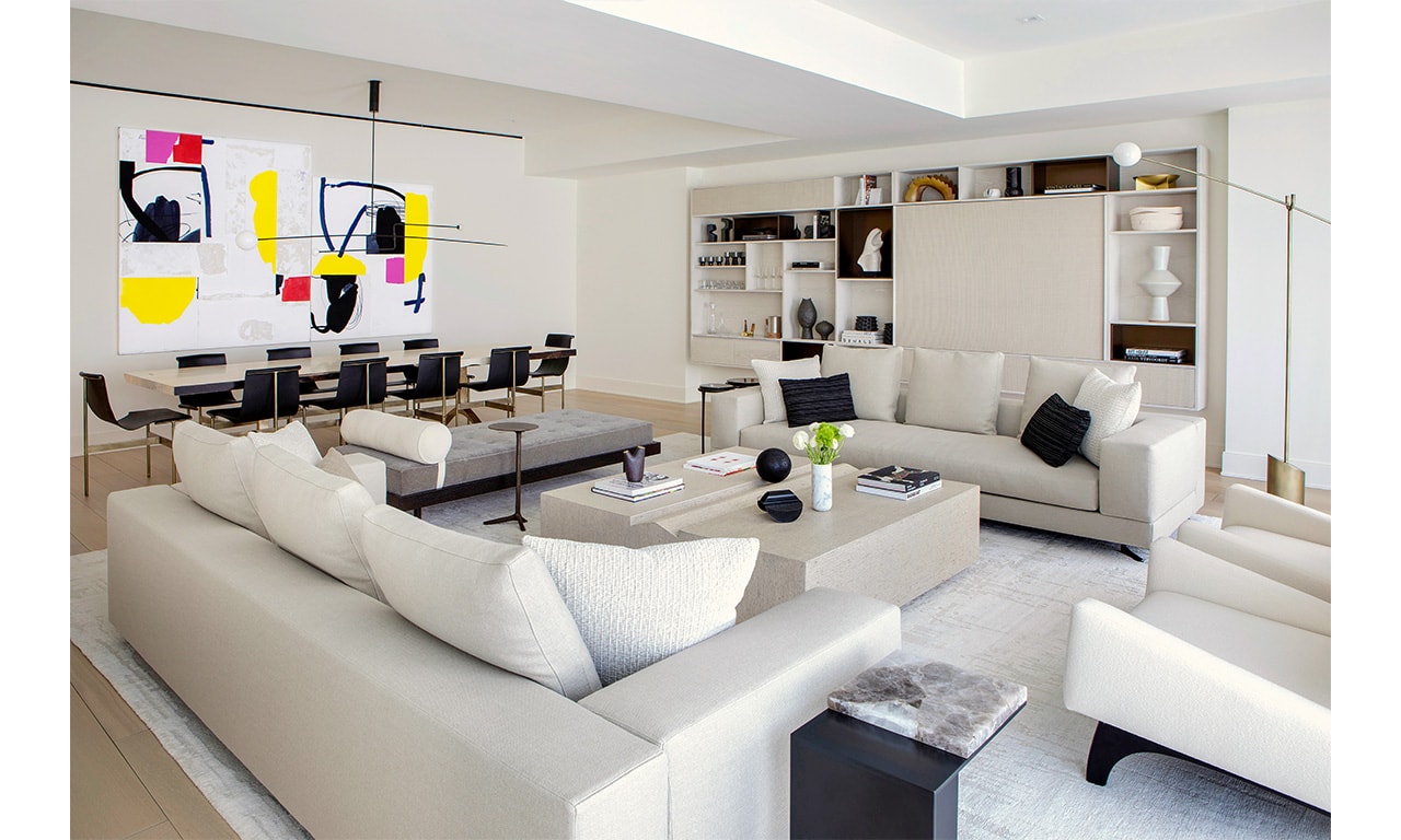 A contemporary open-concept living and dining area with plush white sofas, a neutral coffee table, and a striking abstract painting adding a pop of color