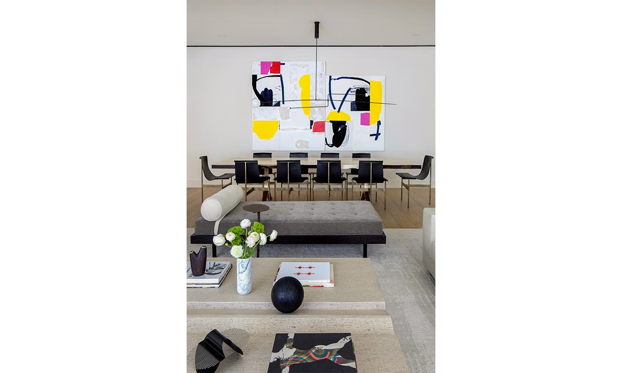 A modern living and dining space featuring a bold abstract painting, sleek black chairs, and a neutral-toned coffee table adorned with elegant decor.