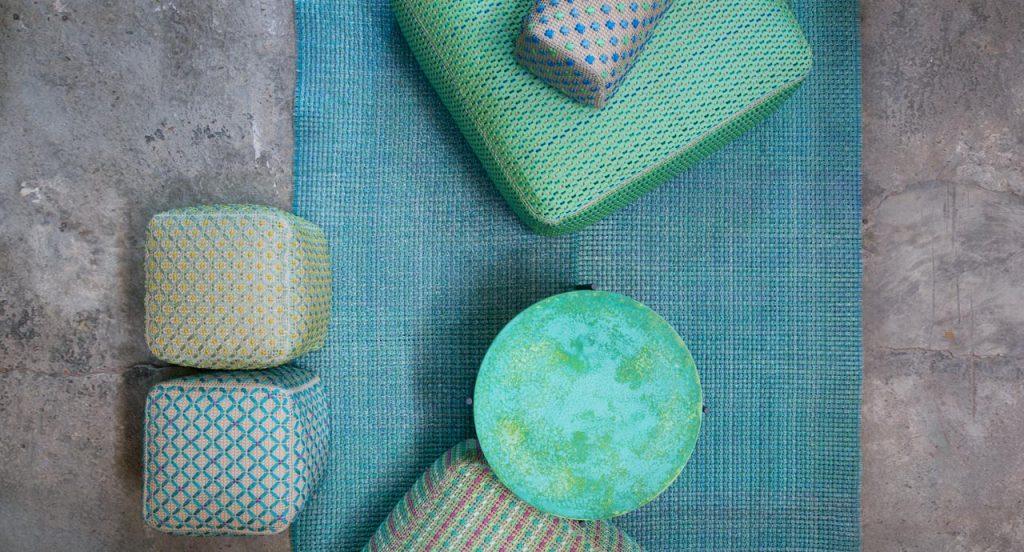 Six Spezie poufs embroidered. Two in blue and green, one in blue, one in yellow and one in blue, red and white in a living room.