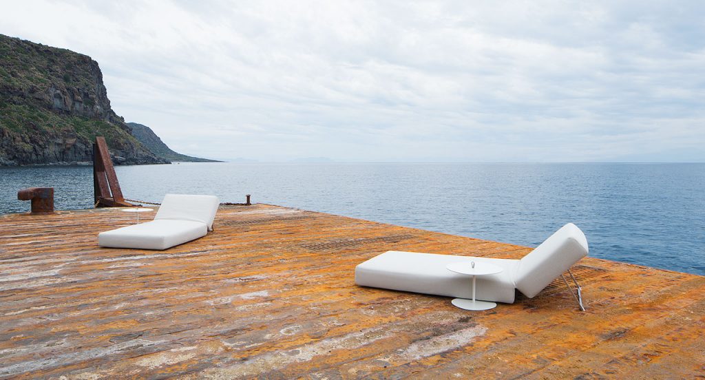Two white round Strap sides tables. Aluminium structure next to a lake.