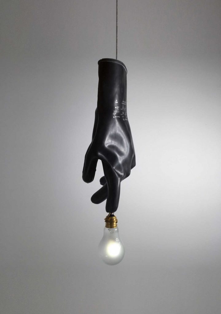 Luzy in black illuminated hanging from a ceiling in front of a white wall