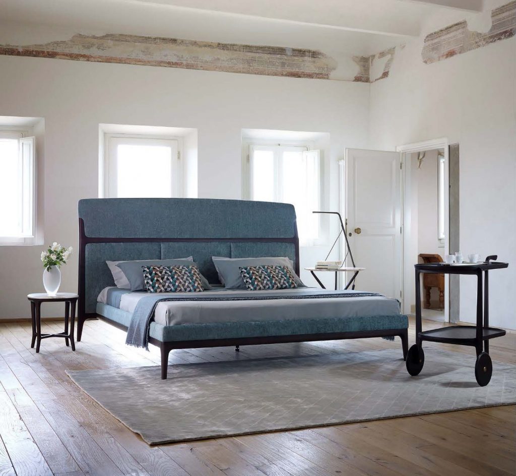 bed made of velvet fabric in a shade of blue with white resting on a wooden base in a room