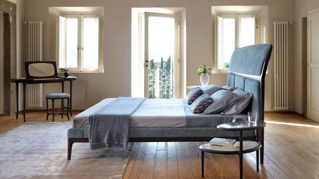 bed made of velvet fabric in a shade of blue with white resting on a wooden base in a room