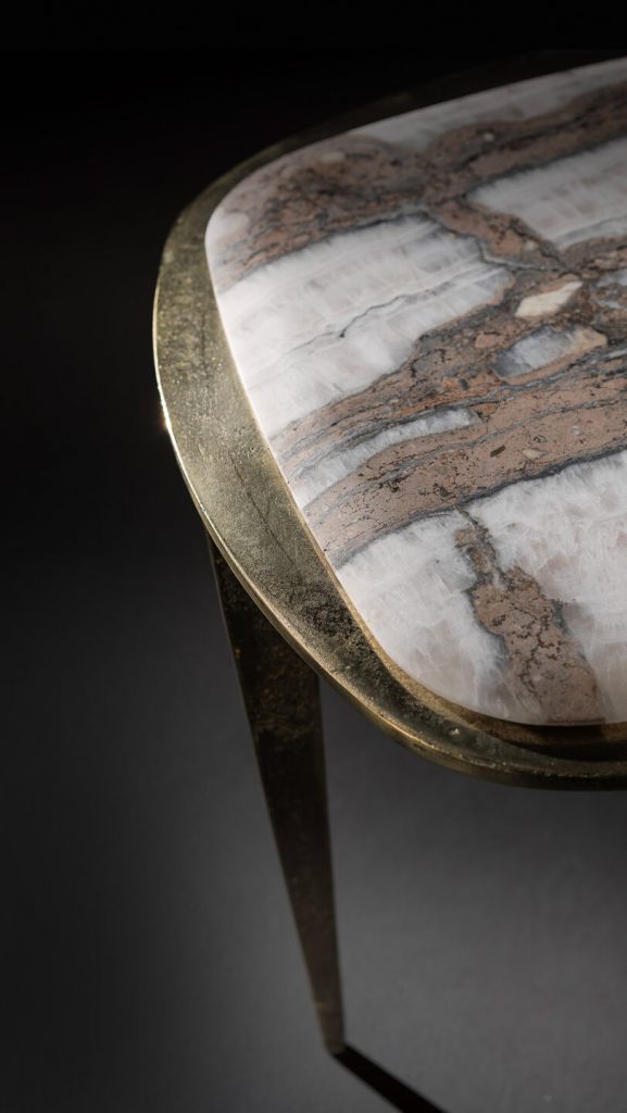 stool top made of white titanium stone resting on a burnished brass base on a gray background