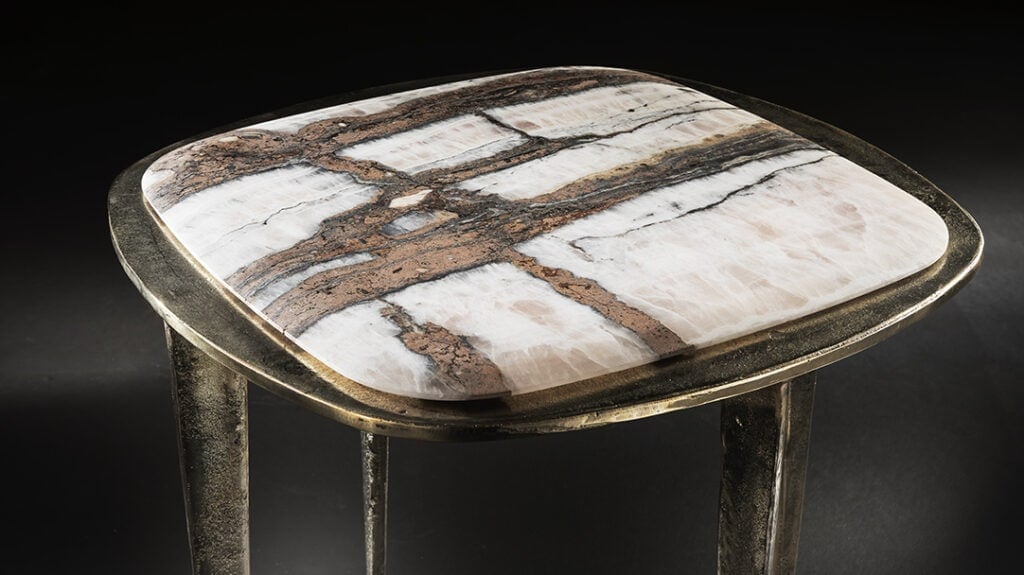 stool top made of white titanium stone resting on a burnished brass base on a gray background