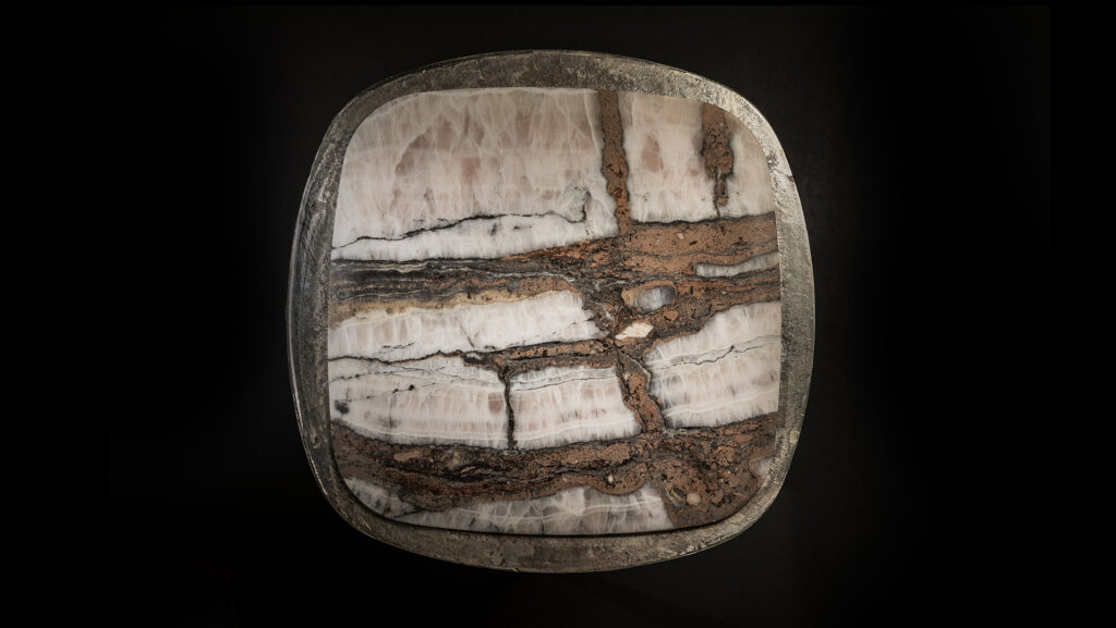 stool top made of white titanium stone resting on a burnished brass base on a gray background