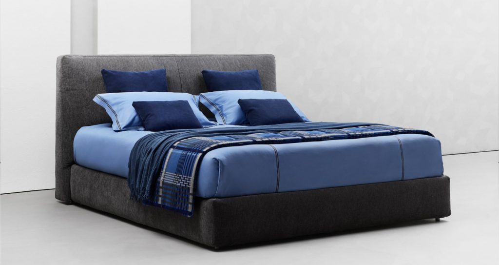 Modern double bed made with a high and thick headboard, richly padded in a dark gray tone on a white background