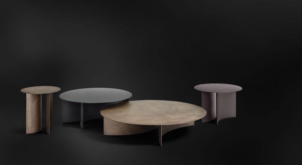 round tables in four sizes made of metal top and curved base in matte burnished, rust and black color tones on a black background