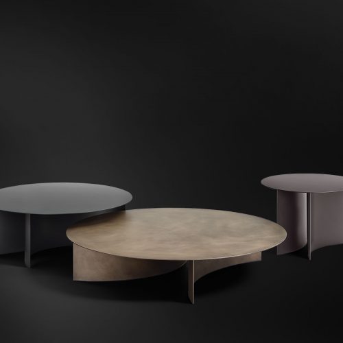 round tables in four sizes made of metal top and curved base in matte burnished, rust and black color tones on a black background