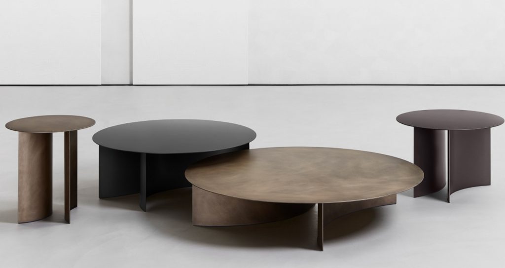 round tables in four sizes made of metal top and curved base in matte burnished, rust and black color tones on a white background