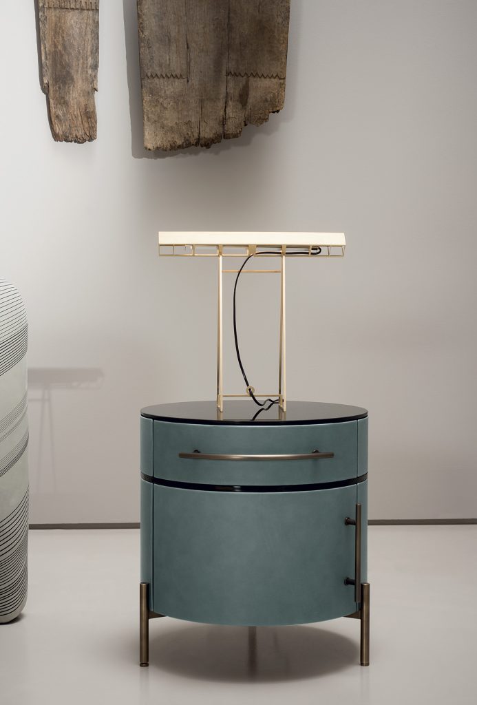 Cylinder-shaped nightstand made of glass, wood and aluminum in a green and gold brown tone in a living room