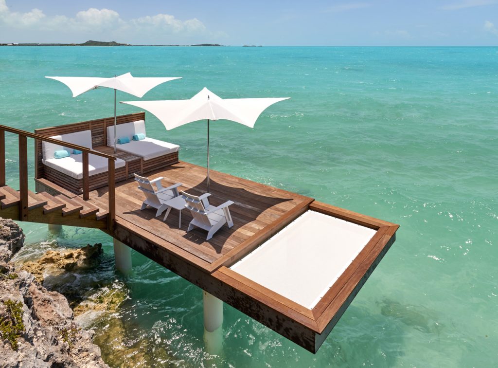 Two parasol with polished titanium structure in the middle and fabric on the top in white color tone on a beach background