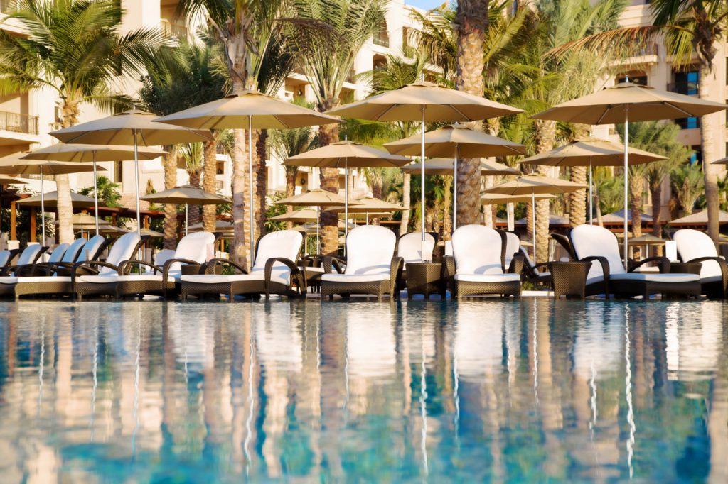 Line of umbrellas with polished titanium structure in the middle and fabric on the top in white tone on a pool background