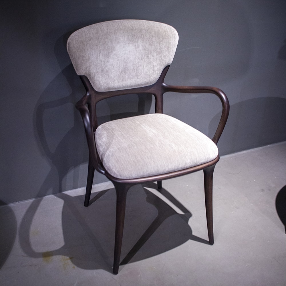 Chair made with a walnut wood base and upholstered in light gray belsuede fabric on a gray background